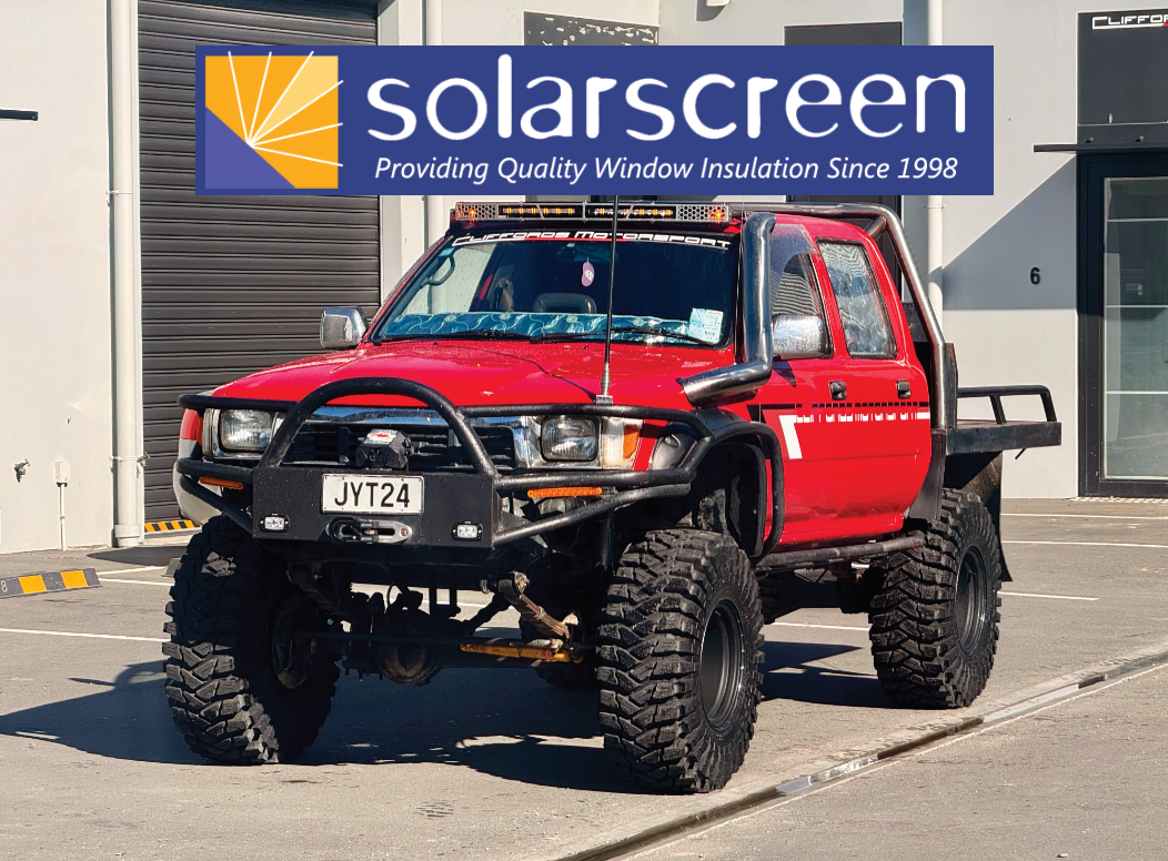 Red pickup truck with 'solarscreen' logo and text on a building.
